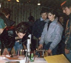 a group of people standing around a table with candles on it and one man blowing out the candles