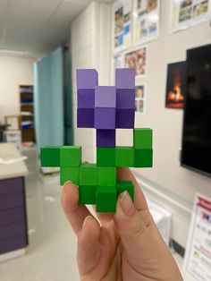 a person holding up a piece of paper in the shape of a purple and green block