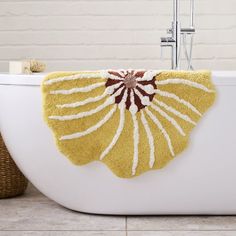 a bathtub with a yellow flower rug on the side and a basket next to it