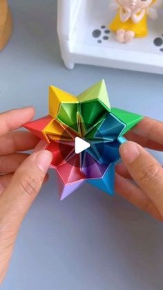 a person is holding a colorful origami star in their left hand, with the other hand reaching for it