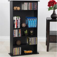 a black bookcase filled with dvd's next to a table and vase full of flowers