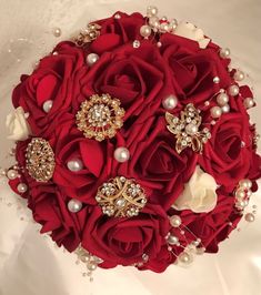 a bridal bouquet with red roses, pearls and brooches on white fabric