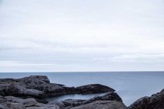 a bench sitting on top of a rock covered beach next to the ocean in front of an overcast sky