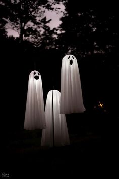 two white ghost lamps in the dark with trees in the back ground and one light is turned on