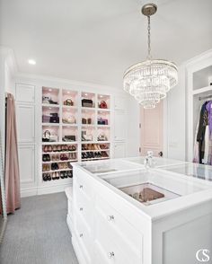 a closet with white cabinets and chandelier hanging from it's ceiling, filled with shoes