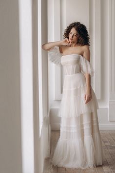 a woman in a white dress leaning against a wall with her hand on her head