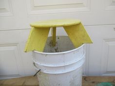 a yellow bench sitting on top of a white bucket in front of a garage door