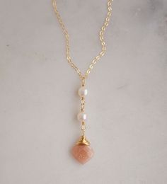 Two white semi-round pearls hang over a natural peach Moonstone faceted drop. The gold style pendant is shown. Pearl Necklaces With Faceted Detail As Gift, Peach Pearl Drop Jewelry As Gift, Peach Pearl Drop Jewelry Gift, Peach Pearl Drop Jewelry For Gift, Gold Faceted Pearl Necklace Gift, Peach Pearl Jewelry As Gift, Peach Pearl Jewelry For Gift, Peach Pearl Jewelry For Gifts, Wedding Jewelry Simple