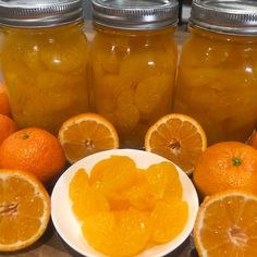 several jars filled with oranges sitting on top of a counter next to sliced oranges