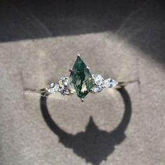 an engagement ring with a green and white stone surrounded by smaller stones on the side