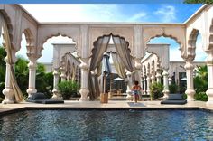 a woman sitting on the edge of a pool in front of an outdoor gazebo