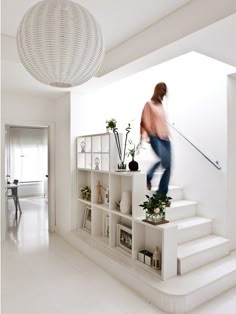 a woman is walking up the stairs in her living room with plants and bookshelves