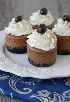 four chocolate cupcakes with white frosting and black olives on top sitting on a plate