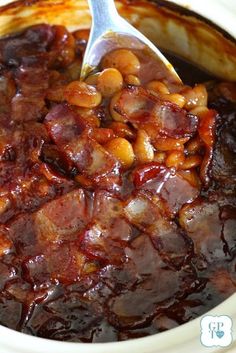 a spoon is in a bowl full of beans and meats with sauce on it