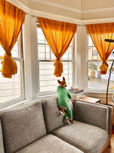 a stuffed animal sitting on top of a gray couch in front of two large windows