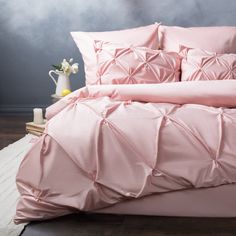 a bed with pink sheets and pillows on top of wooden flooring next to a white vase