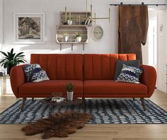 a living room with an orange couch and rugs on the wooden floor, shelving above it