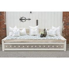 a white bench with pillows and a teapot on it in front of a brick wall