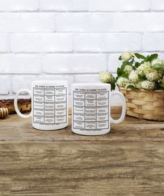 two coffee mugs sitting next to each other on top of a wooden table with flowers