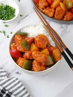 two bowls filled with chicken and vegetables next to chopsticks on a white table