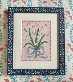 a blue frame with flowers and birds on it sitting on a floral wallpapered surface