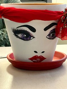 a cup with a face painted on the side and a red bow around its head