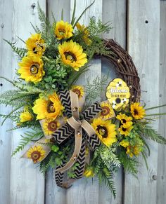 a wreath with sunflowers and greenery hanging on a fence