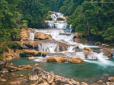 a man standing in the middle of a river next to rocks and water cascading