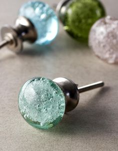 three different colored glass door knobs on a counter top with silver and green handles