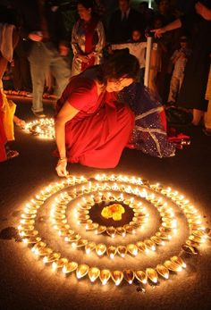 a woman kneeling down on the ground in front of a circle of candles with people standing around