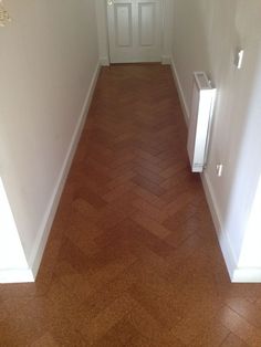 an empty hallway leading to a white door and brown tile floor with herringbone pattern on the floor