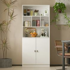 a white bookcase with plants and books on it next to a dining room table