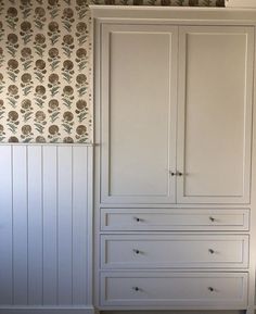 a white armoire sitting next to a wallpapered wall with flowers on it