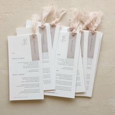 five wedding program cards with ribbons tied to the top and bottom, on a beige background