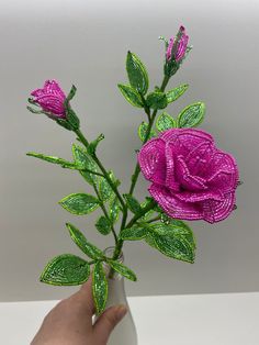 a hand is holding a pink rose with green leaves on it and sequins