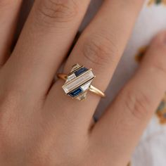 a close up of a person's hand wearing a gold ring with blue and white stones