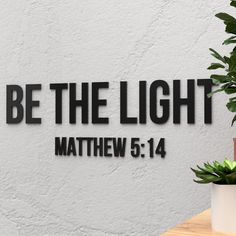 a sign that says be the light with a plant next to it