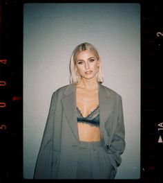 a woman with blonde hair wearing a gray suit and black bra in front of a white wall