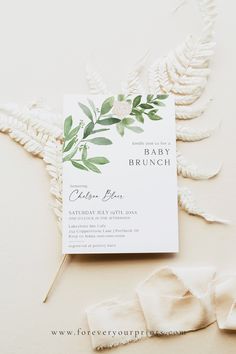 the wedding stationery is laid out on top of white fabric and has green leaves