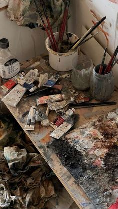 an artist's desk with lots of paint and brushes