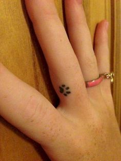 a person's hand with a small dog paw tattoo on their left thumb and finger