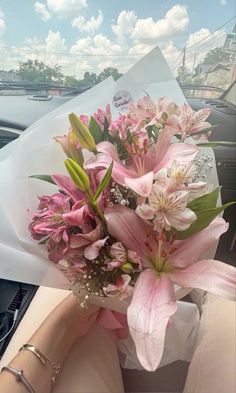 a bouquet of pink flowers sitting in the passenger seat of a car with someone's hand holding it