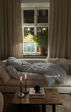 a living room with a couch, coffee table and two candles in front of the window