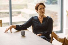 a woman sitting at a table with a coffee cup in front of her and looking off to the side