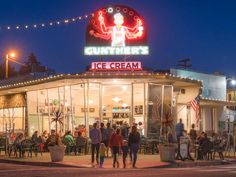 a group of people standing in front of a ice cream shop at night with lights on