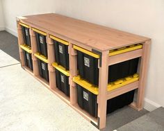 a wooden shelf filled with black and yellow plastic bins next to a white wall