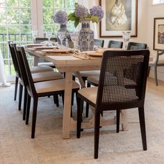 a dining room table with chairs and pictures on the wall in front of it's windows