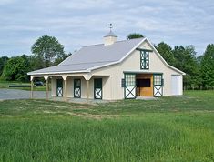 a large white barn with green trim and windows on the front, surrounded by tall grass