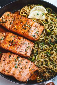 salmon and noodles in a skillet with lemon wedges on the side for garnish