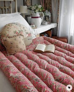 an open book is laying on a bed with pink and green floral bedspread